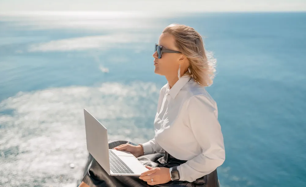 Female digital nomad with laptop overlooking the sea